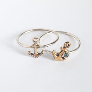 May include: Two silver anchor rings with a gold anchor charm on each. One anchor charm has a small blue gemstone.
