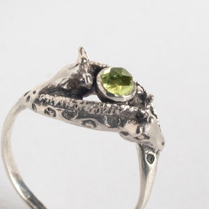 close up of two giraffes ring in silver with rosecut peridot, on a white background