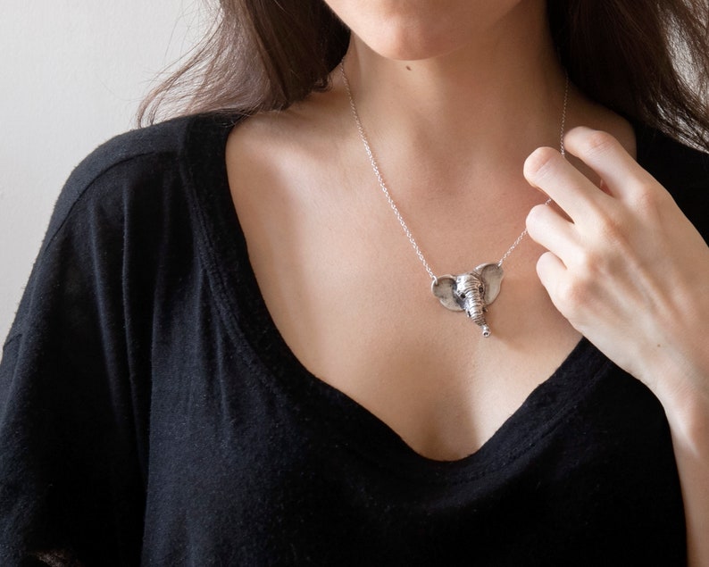 sterling silver elephant head necklace on model wearing black shirt with hand at neck