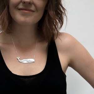 silver whale necklace with etched skeleton, worn by a model wearing a black tank top in front of a white wall