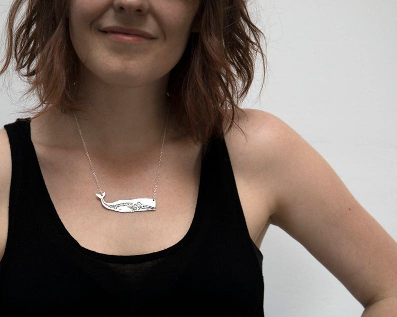 silver whale necklace with etched skeleton, worn by a model wearing a black tank top in front of a white wall