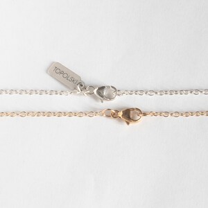 close up shot of lobster clasps on cable chains, one silver and one gold.