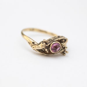 14k gold double giraffe head ring, with rose cut rhodolite garnet, laying on white background