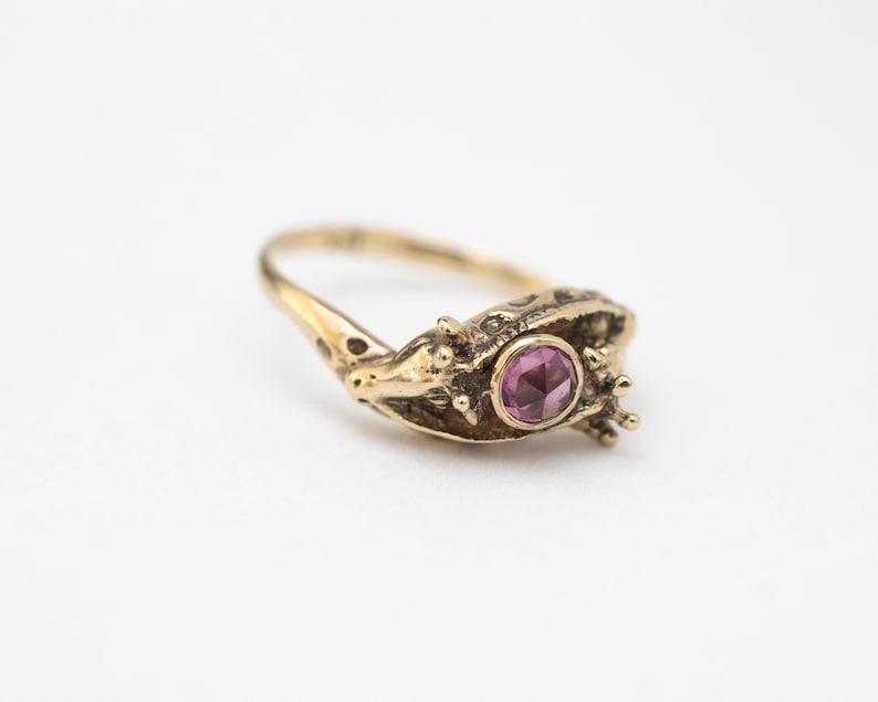 14k gold double giraffe head ring, with rose cut rhodolite garnet, laying on white background