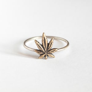 May include: A silver ring with a gold marijuana leaf design.