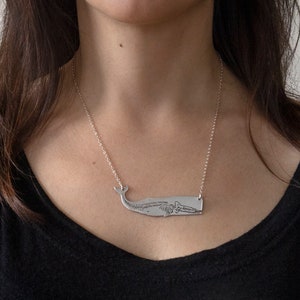 silver whale necklace with etched skeleton, worn by a model wearing a black shirt in front of a white wall