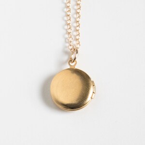 Small gold round locket, on a cable chain. Shown from the back on a white background.