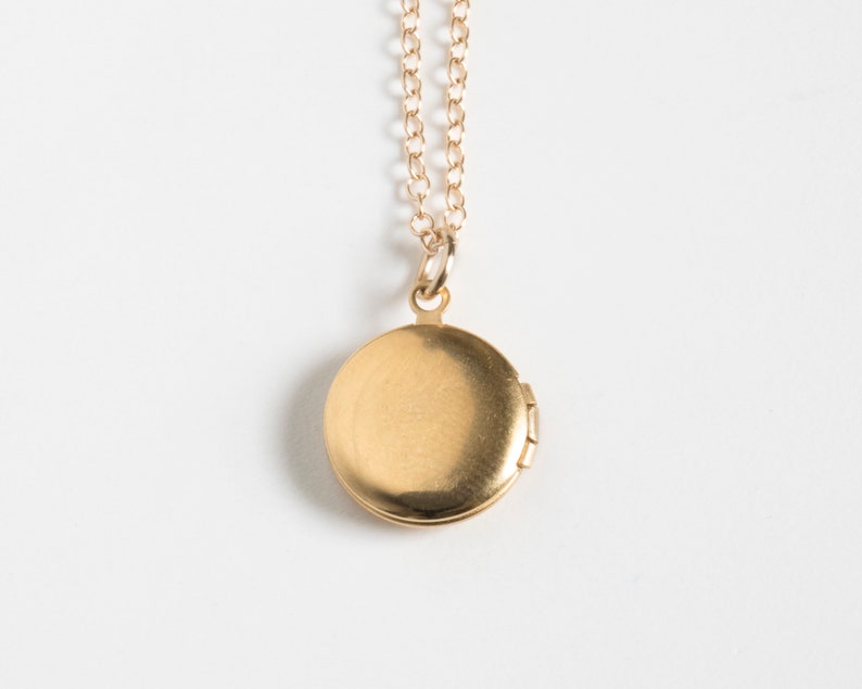 Small gold round locket, on a cable chain. Shown from the back on a white background.