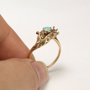 14k gold double giraffe head ring, with opal cabochon, held by fingers on white background