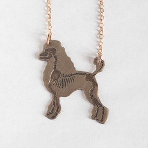 brass poodle silhouette necklace with etched skeleton, shown on a white background