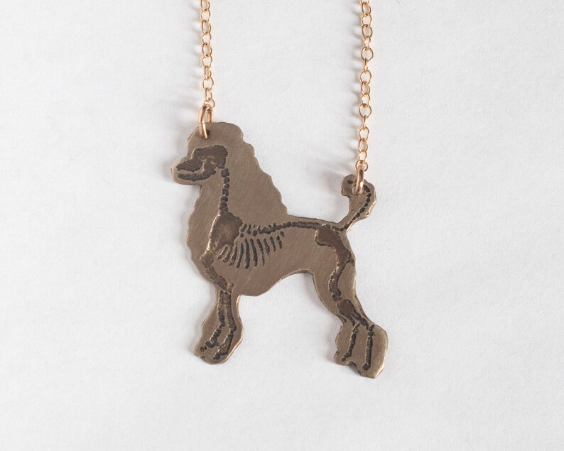 brass poodle silhouette necklace with etched skeleton, shown on a white background