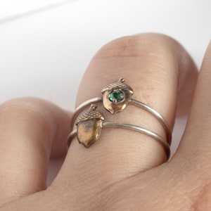 two acorn rings on a single finger, one with an emerald, on a white background