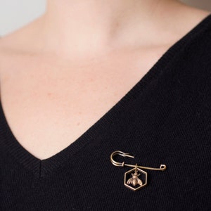 a bee in hexagon brass pin worn on a black sweater