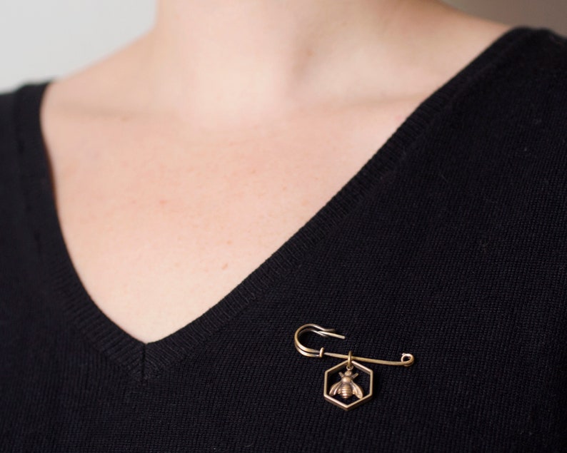 a bee in hexagon brass pin worn on a black sweater