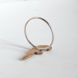 brass parrot charm on a thin silver band. laying face down on a white surface