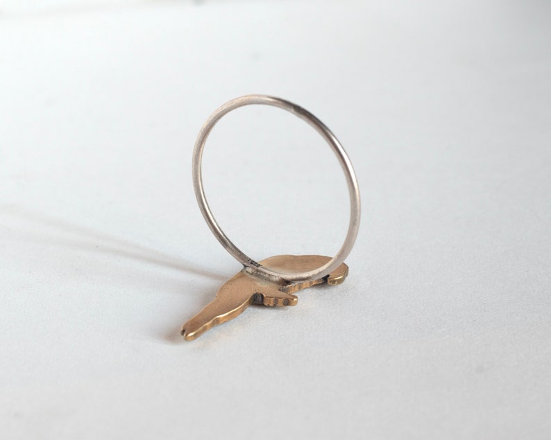 brass parrot charm on a thin silver band. laying face down on a white surface