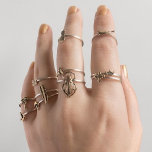 hand wearing many various brass charm rings, held up in front of white background