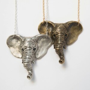 two elephant head pendants, in brass and silver on white background