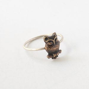 brass owl ring with a thin silver band. At an angle on a white background.