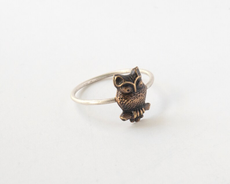 brass owl ring with a thin silver band. At an angle on a white background.