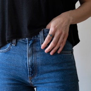 London blue oval gemstone ring, with a brass bee on each side. Shown on a model's hand tucked into jeans, on a white background.
