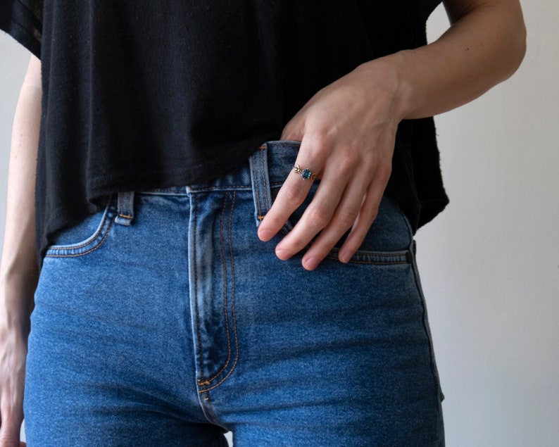 London blue oval gemstone ring, with a brass bee on each side. Shown on a model's hand tucked into jeans, on a white background.