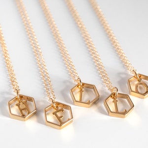 5 gold hexagon pendants with an initial inside, lat an angle on a white background to spell "hello"