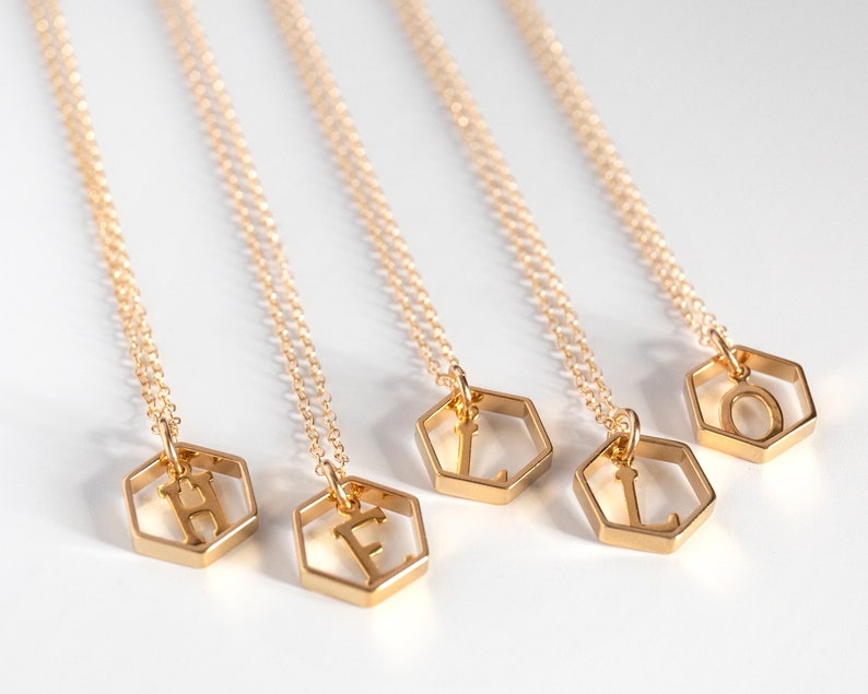 5 gold hexagon pendants with an initial inside, lat an angle on a white background to spell "hello"