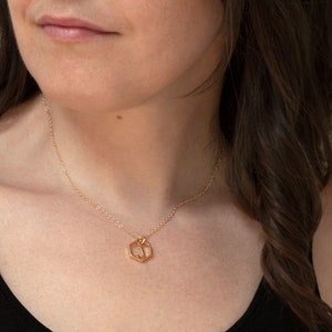 model wearing a gold hexagon pendant with an initial inside and a black tank top. in front of white wall