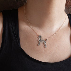 silver poodle silhouette necklace with etched skeleton, worn by a model wearing a black tank top in front of brick wall.