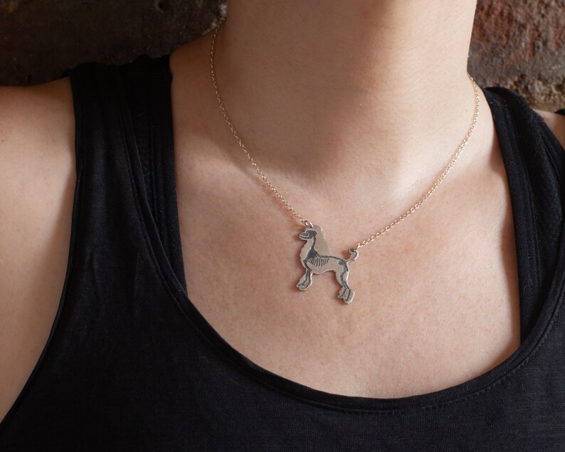 silver poodle silhouette necklace with etched skeleton, worn by a model wearing a black tank top in front of brick wall.