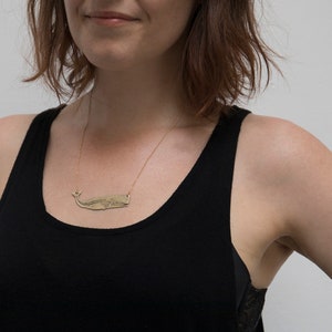 brass whale necklace with etched skeleton, worn by a model wearing a black tank top in front of a white wall