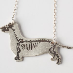 brass dachshund pendant with etched skeleton, close-up on white background.