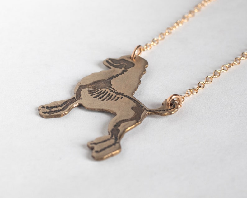 brass poodle silhouette necklace with etched skeleton, shown at an angle on a white background