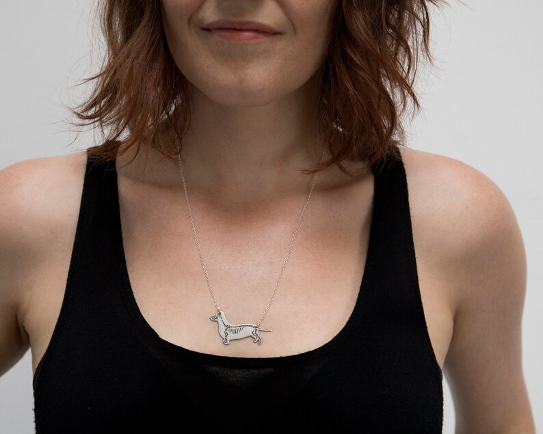 silver dachshund pendant with etched skeleton, worn by a model wearing black tank top with white background.
