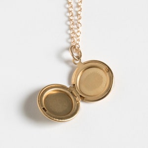 Small gold round locket, shown open on a cable chain, on a white background.