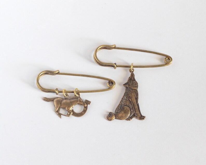 a brass horse and horseshoe pin, and a howling wolf charm pin on a white background