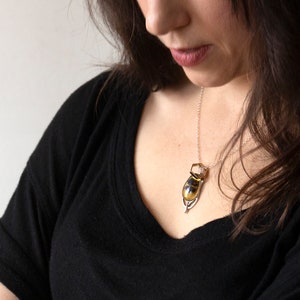 Real honeybee preserved in resin with gold backing in a teardrop shape. Set into a hand carved silver pendant in an art deco style. Worn by a model wearing a black tee with white background.