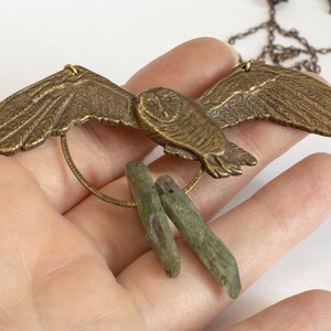 brass barn owl necklace with rough kyanite, held in a hand