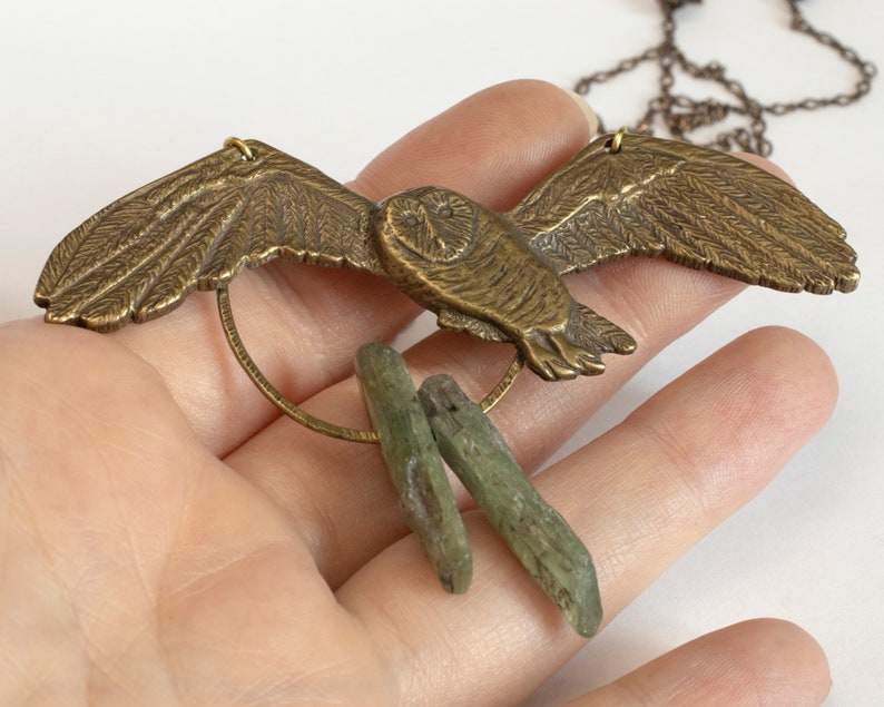 brass barn owl necklace with rough kyanite, held in a hand