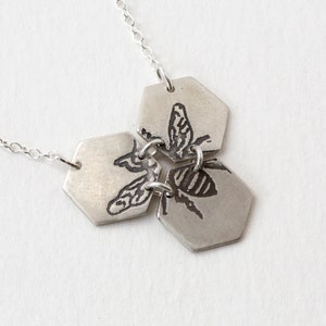 three silver hexagons pendant with etched bee, at an angle on white background