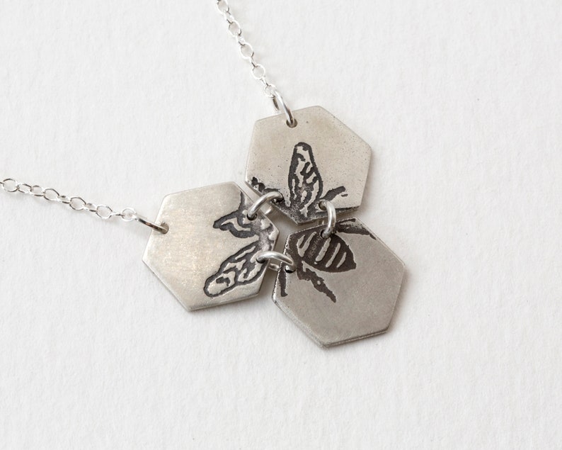 three silver hexagons pendant with etched bee, at an angle on white background