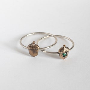 two acorn rings, one with an emerald and one without, on a white background