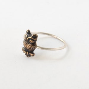 Round brass owl ring with a thin silver band. At an angle on a white background.