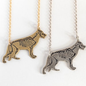 May include: Two necklaces with a German Shepherd skeleton pendant. One necklace has a gold chain and the other has a silver chain.