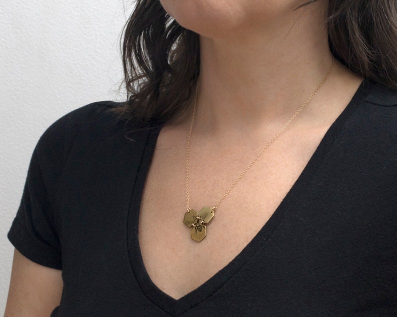 three brass hexagons pendant with etched bee, on a model with white background