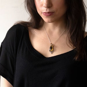 Real honeybee preserved in resin with gold backing in a teardrop shape. Set into a hand carved pendant in an art deco style. Worn by a model wearing a black tee with white background.