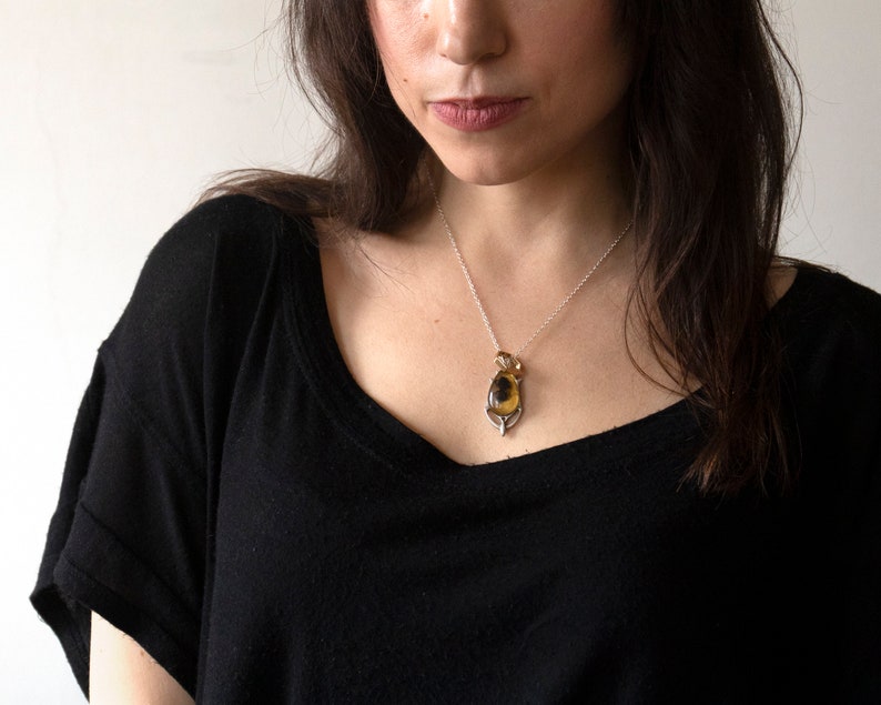 Real honeybee preserved in resin with gold backing in a teardrop shape. Set into a hand carved pendant in an art deco style. Worn by a model wearing a black tee with white background.