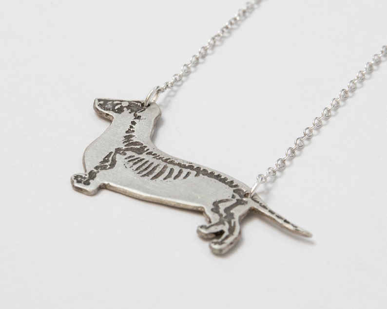 silver dachshund pendant with etched skeleton, at an angle on white background.