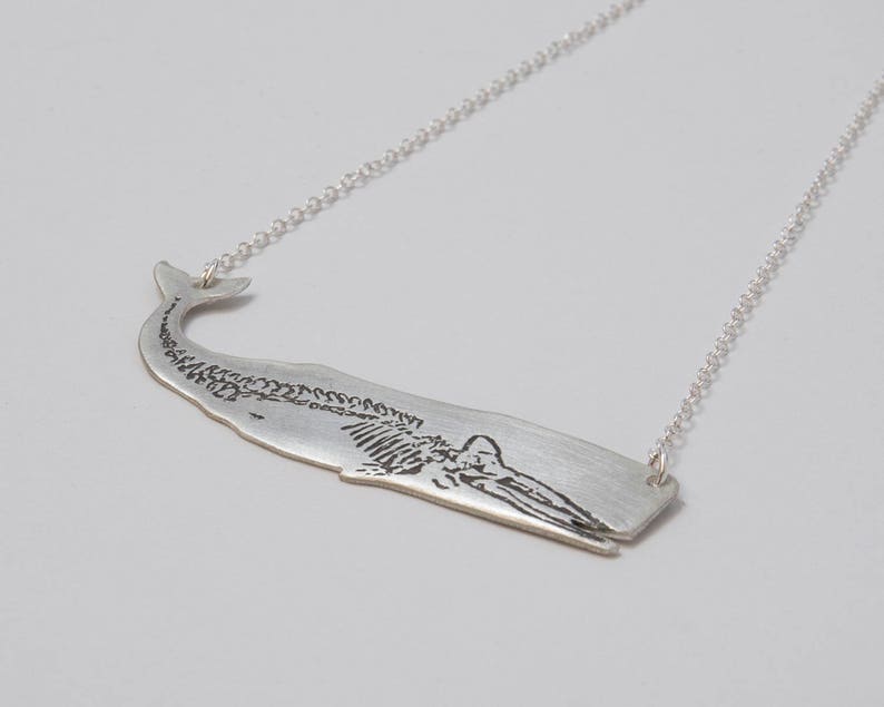 oxidized sterling silver whale pendant with etched skeleton, at an angle on a white background